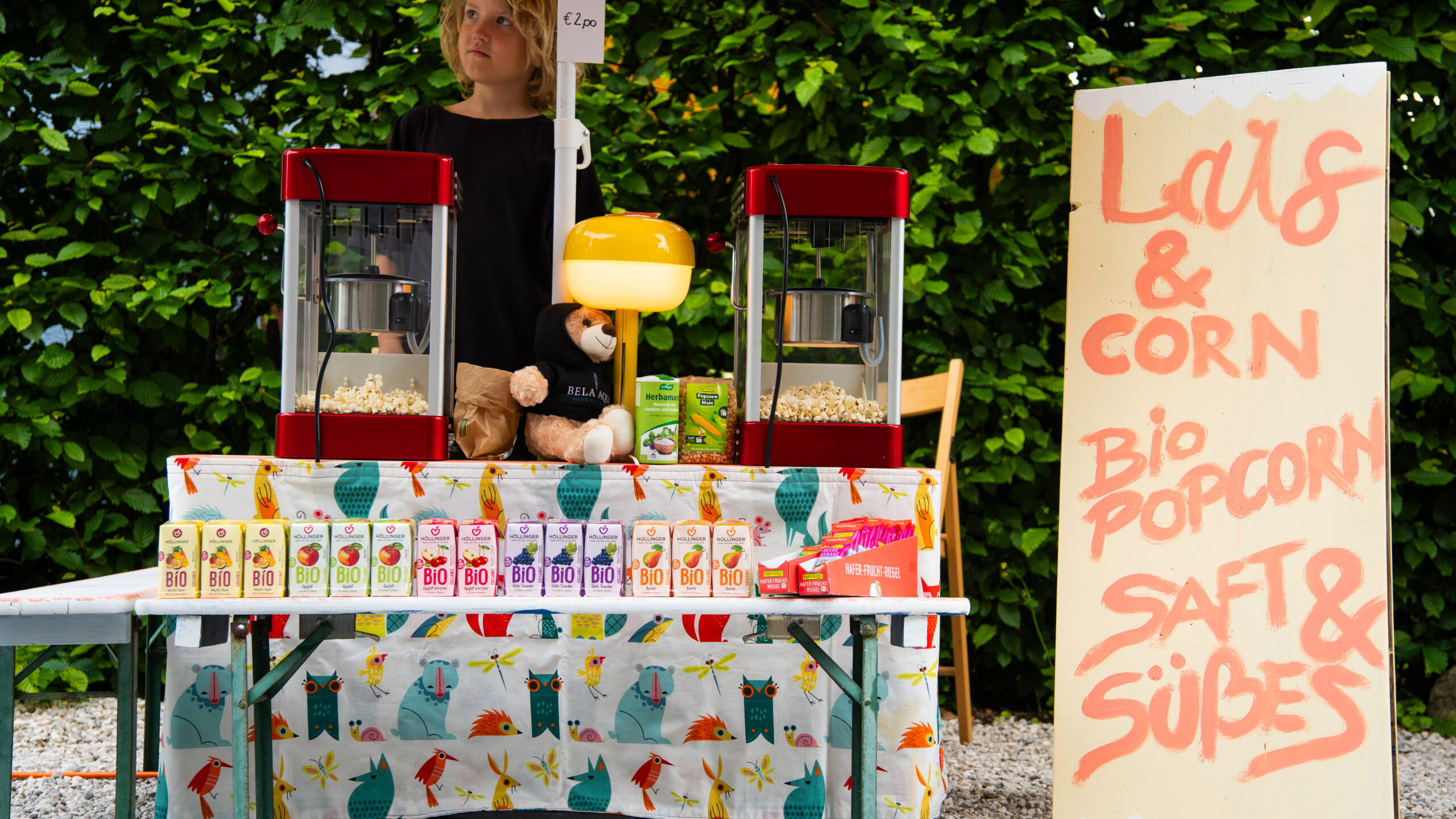 Lars bereitet frisches Bio-Popcorn an einem bunten Verkaufsstand mit Popcornmaschinen und Bio-Säften zu.
